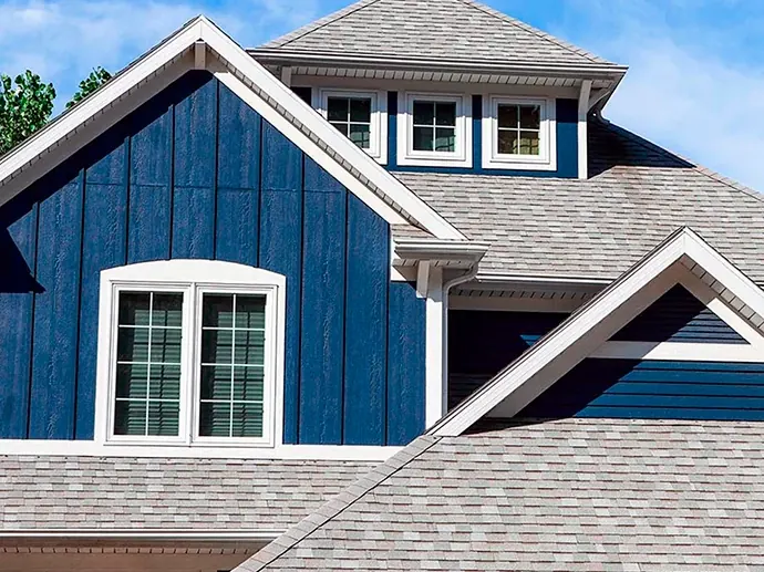 Blue house with white trim and a gray shingle roof under a blue sky